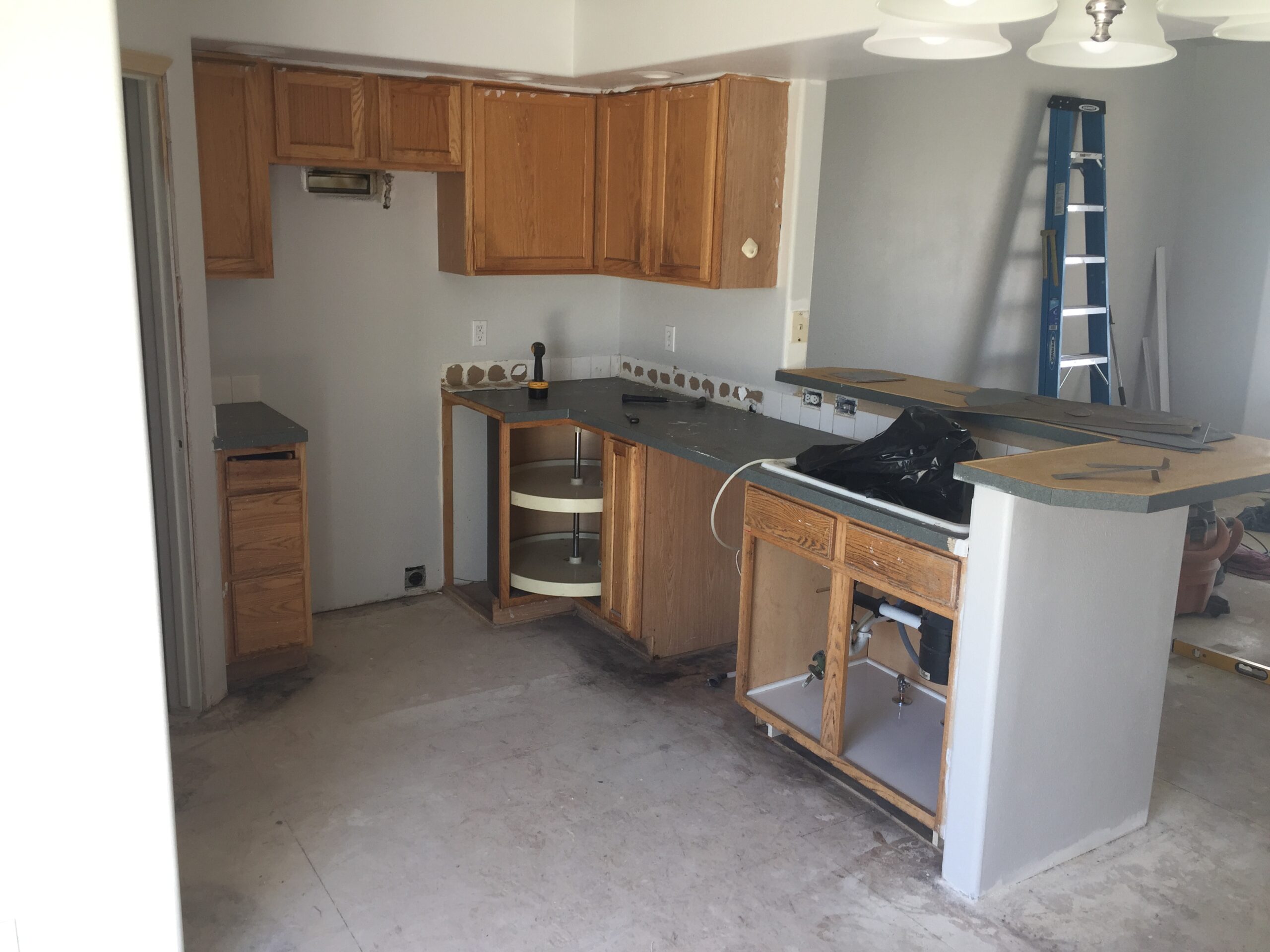 Renovated Kitchen Showing Wooden Cabinets, a Bare Countertop, and an Unfinished Island. A Ladder Is Visible, Indicating Ongoing Remodeling.