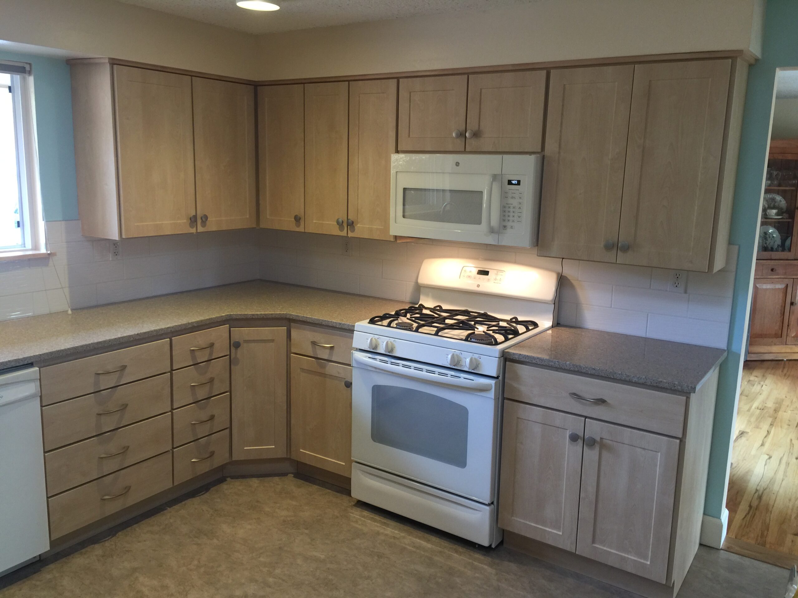 Modern Kitchen With Light Wood Cabinetry, a Gas Stove, and a Microwave. This Updated Design Highlights Functionality and Style, Ideal for Cooking.