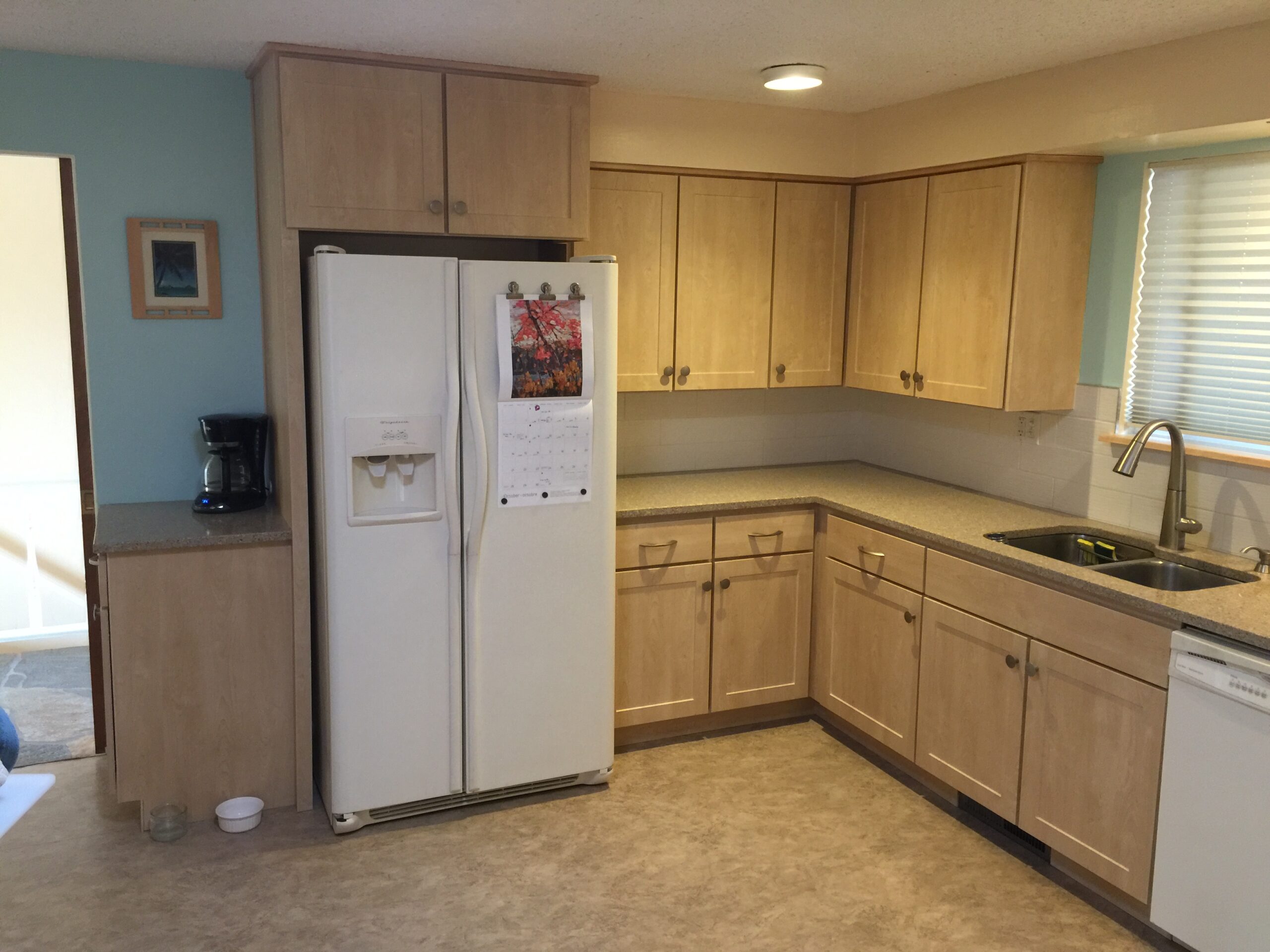 Bright Kitchen Featuring Light Wood Cabinetry, a Refrigerator, a Sink, and a Dishwasher. The Open Layout Enhances Accessibility and Functionality.