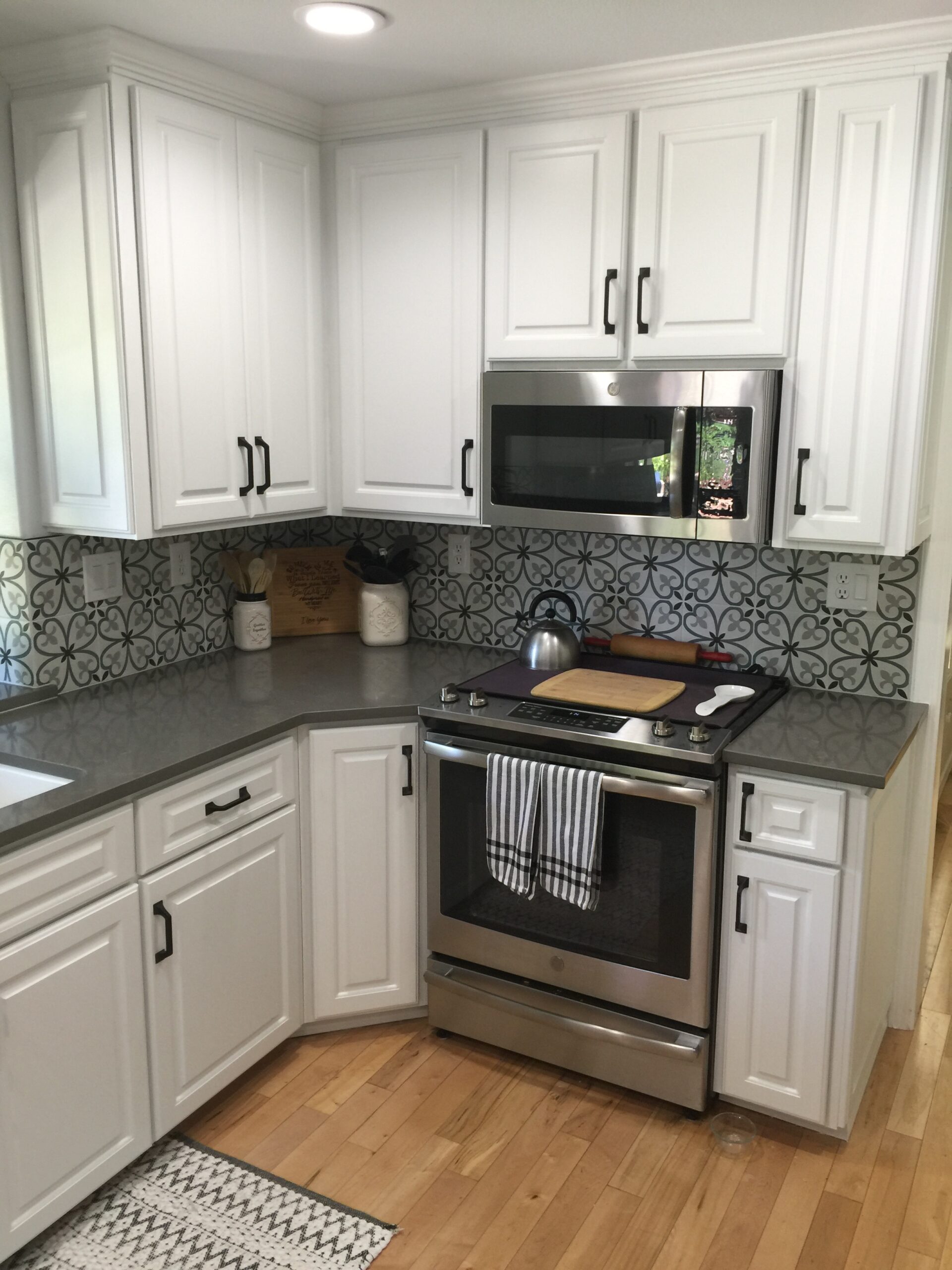 Modern Kitchen Featuring White Cabinetry, a Stainless Steel Oven, and a Microwave Above. A Patterned Backsplash and Hardwood Floor Complete the Inviting Space.